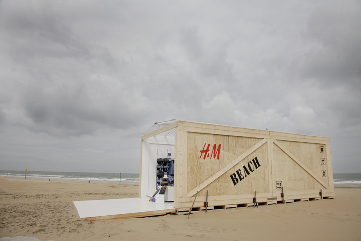 H&M pop-up store on the beach with a light wooden structure, minimalist design and open concept facing the sea.